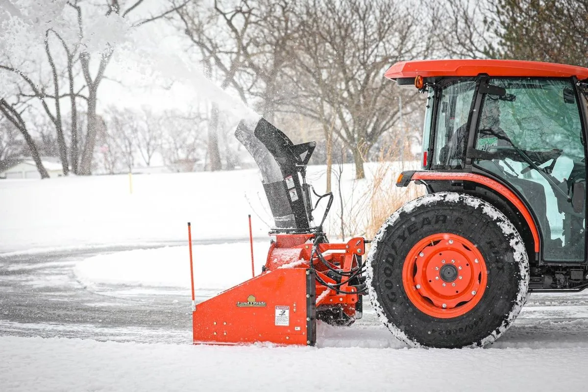 Close view of a tractor snow blower chute throwing snow while the tractor works through fresh snowfall
