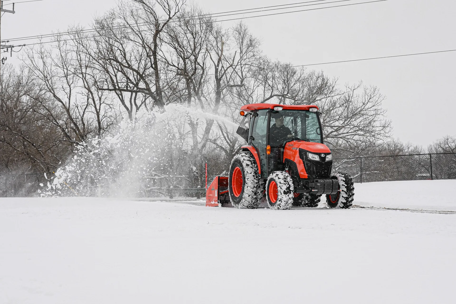 Tractor-mounted snow blower throwing snow in a high arc off to the side